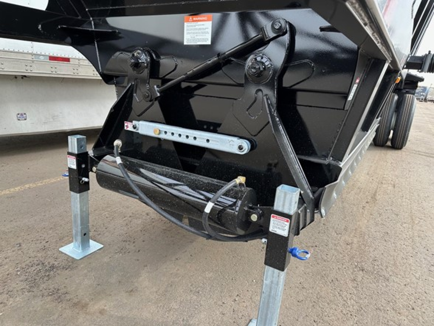 Dump trailer hitch area showing electric ta control, legs/landing gear, and hydraulic lines with a black frame and mounting hardware.