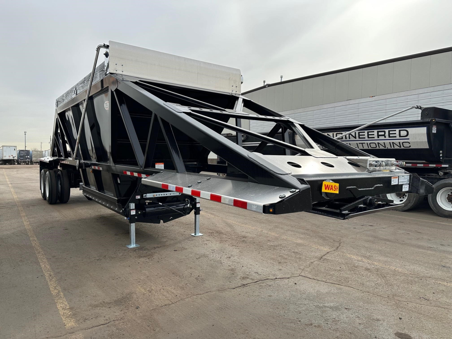 Bottom dump trailer in service position with triangular truss frame and tandem axles showing with a raised hopper and front landing legs.