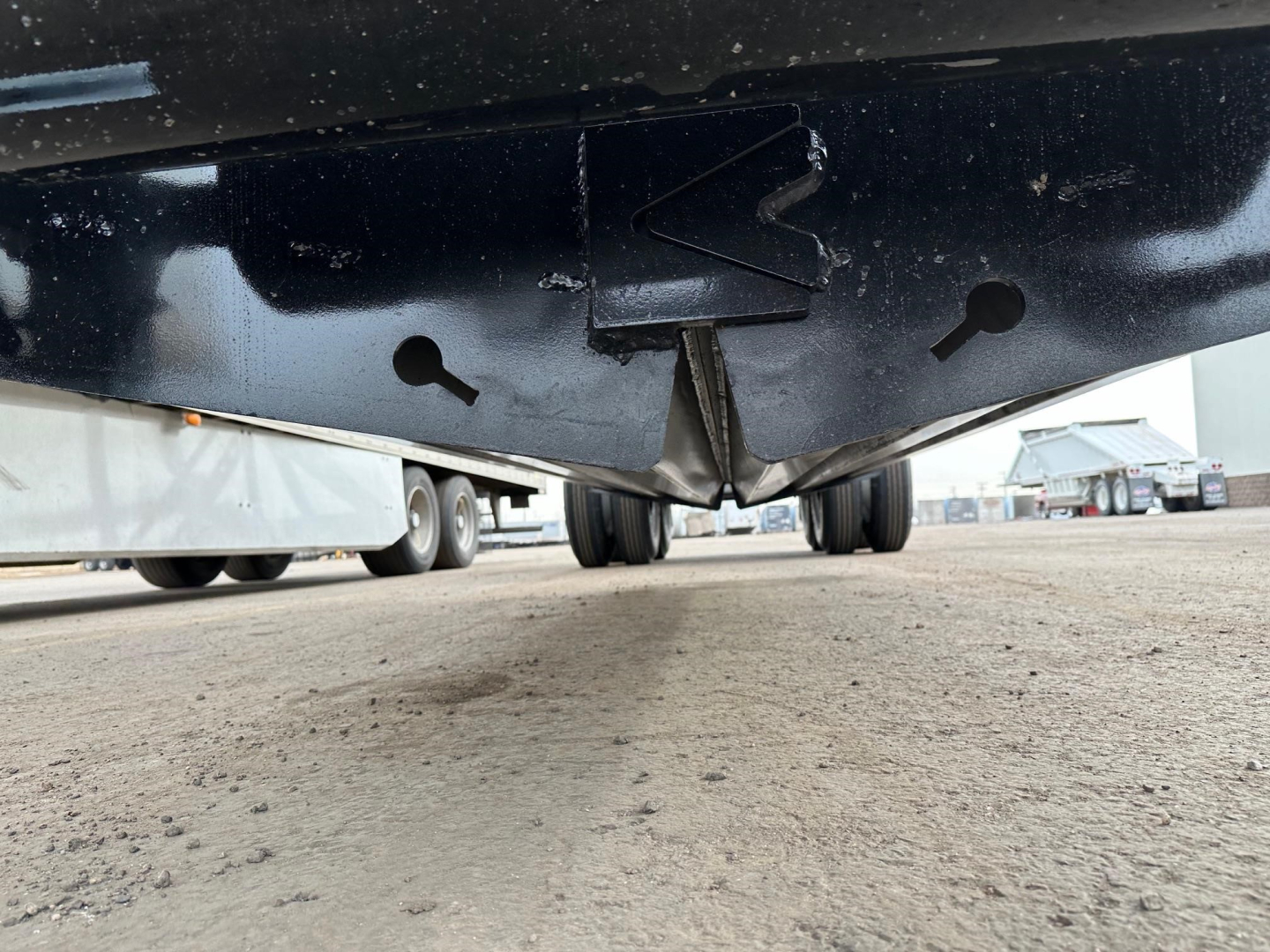 Underbelly of a bottom dump trailer showing the underside with a pointed hitch area and wheels in the distance.