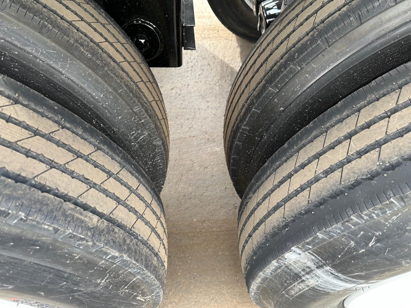 Tire-side view of a dump trailer with dual rear axles showing four tires and part of the frame; no legible text or numbers visible.