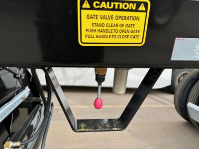 Trailer hitch area showing yellow caution label and bottom dump gate mechanism with pink pin, electric ta -- view of gate valve and handle in center.