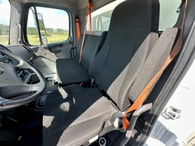 Cab interior of a 2024 Freightliner M2-106 box truck showing two front seats and bench behind, steering wheel, orange seat belts, and side door window.