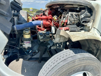 Truck engine bay showing coolant hoses, red engine components, air intake, filter canister, and large front tire in view.