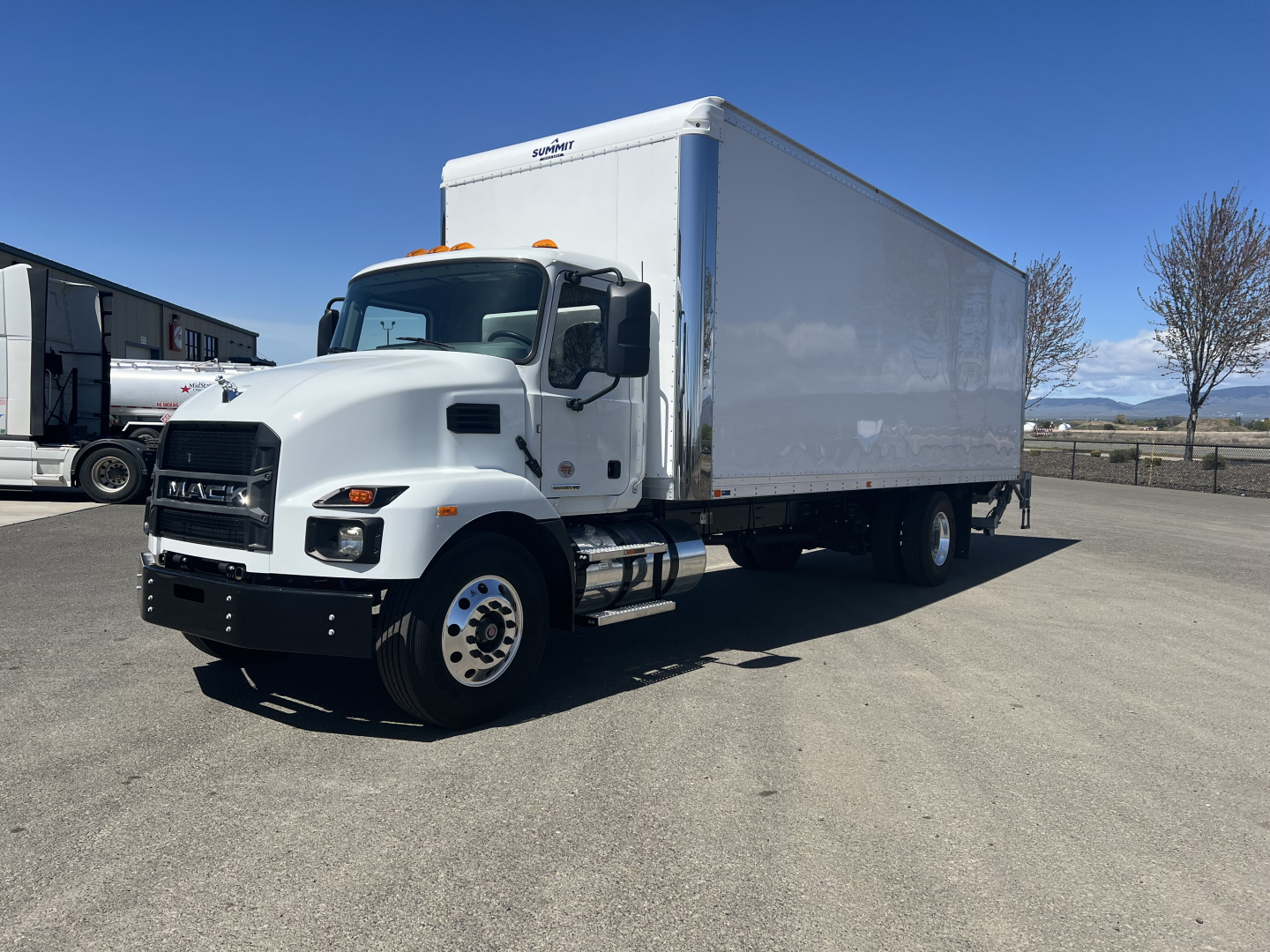 Mack MD6 box truck in a parking lot showing side of large white cargo box and front grille with Mack logo.