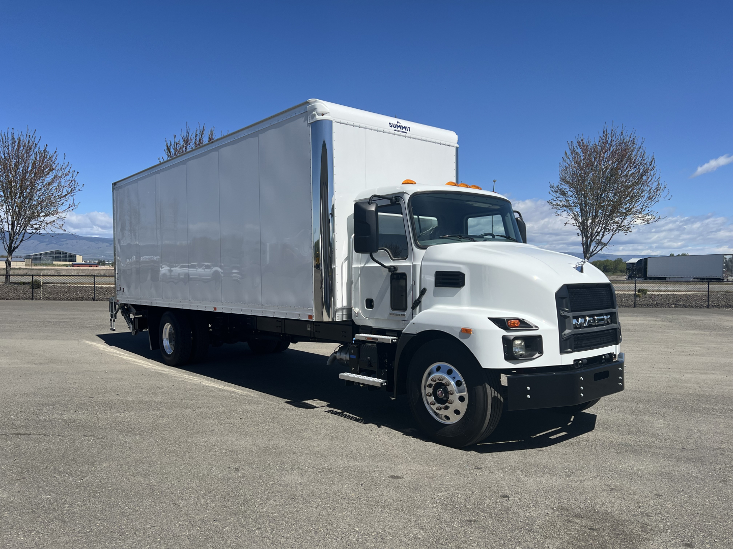 Mack MD6 box truck with white cab and cargo box, side view, clear sky.