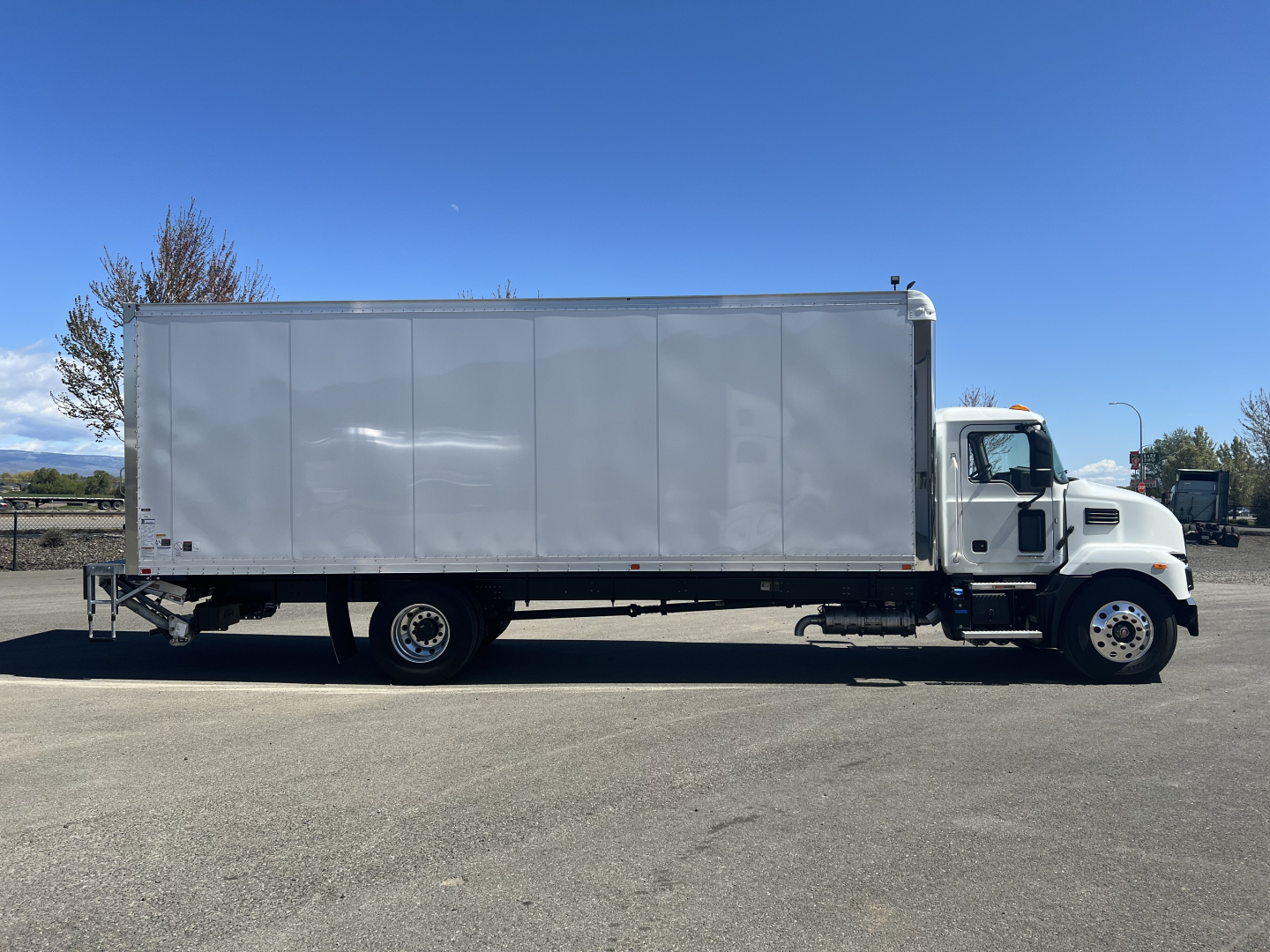 Box truck in side view showing cargo box and cab with Mack MD6 style; white truck with long rectangular cargo area and standard dual rear tires.