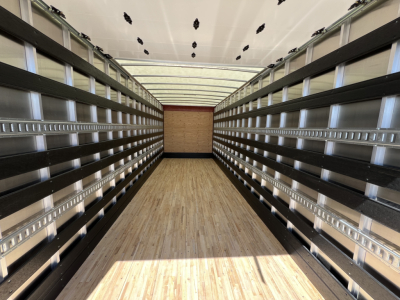Truck trailer interior showing empty cargo space with wooden floor and side rails, viewed from rear doors open.