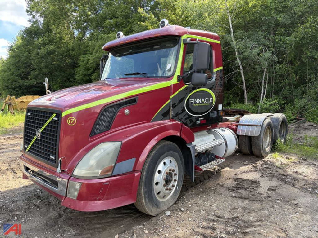 Volvo VNL tractor cab in red with yellow reflective stripes, front grille visible, spare tire mounted on the passenger side, dual rear axles, showing Pinnacle logo on the door.