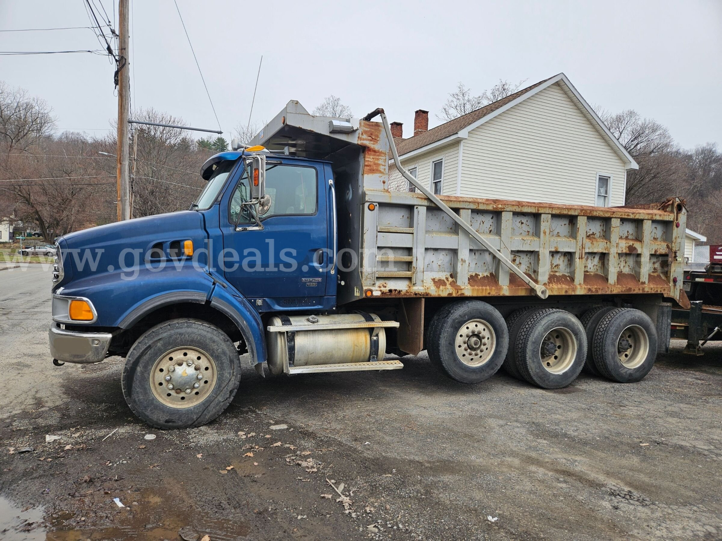 Blue Sterling LT9500 dump truck with rusted dump bed and dual rear axles, side profile view parked on a lot.