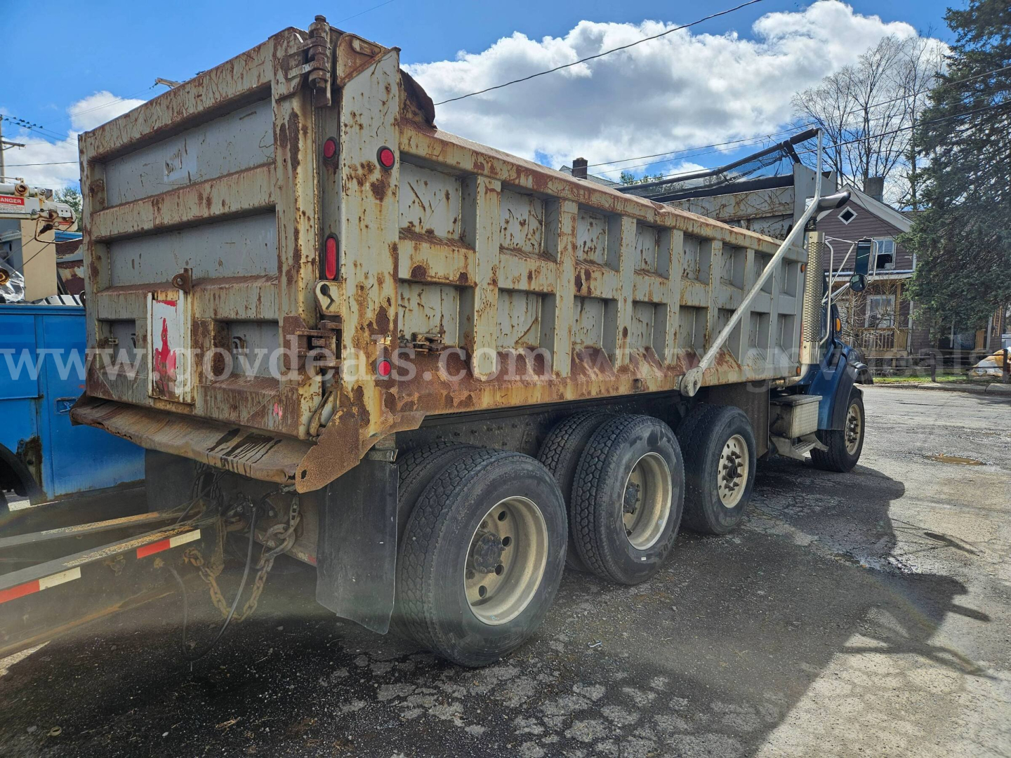 Dump truck, three-axle Sterling LT9500 with a rusted dumping bed, side view showing rear wheels and towing hitch.
