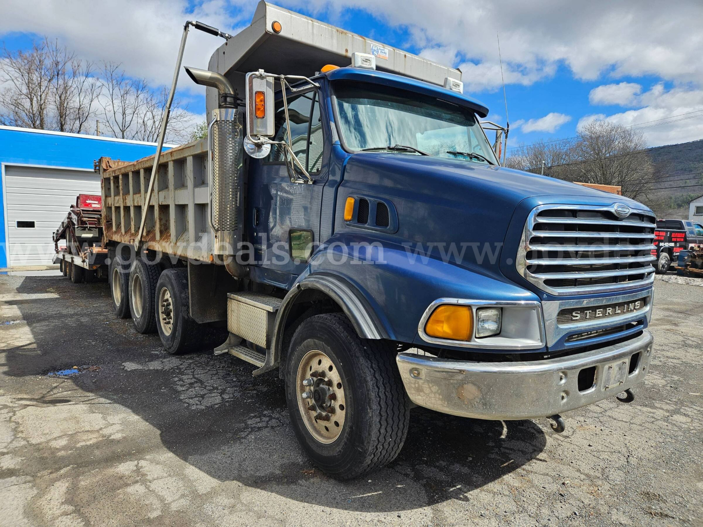 Truck image showing a blue Sterling LT9500 dump truck with a large chrome grille and tip bed, side mirrors, and front bumper.