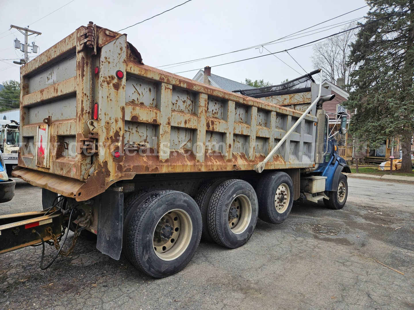 Side view of a rusty dump truck trailer showing weathered metal body and rear wheels.