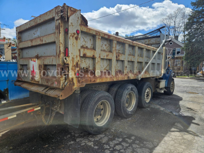 Dump truck, three-axle Sterling LT9500 with a rusted dumping bed, side view showing rear wheels and towing hitch.