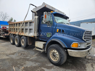 Dump truck in blue cab with open-top dump bed showing Sterling LT9500 logo and front grille.