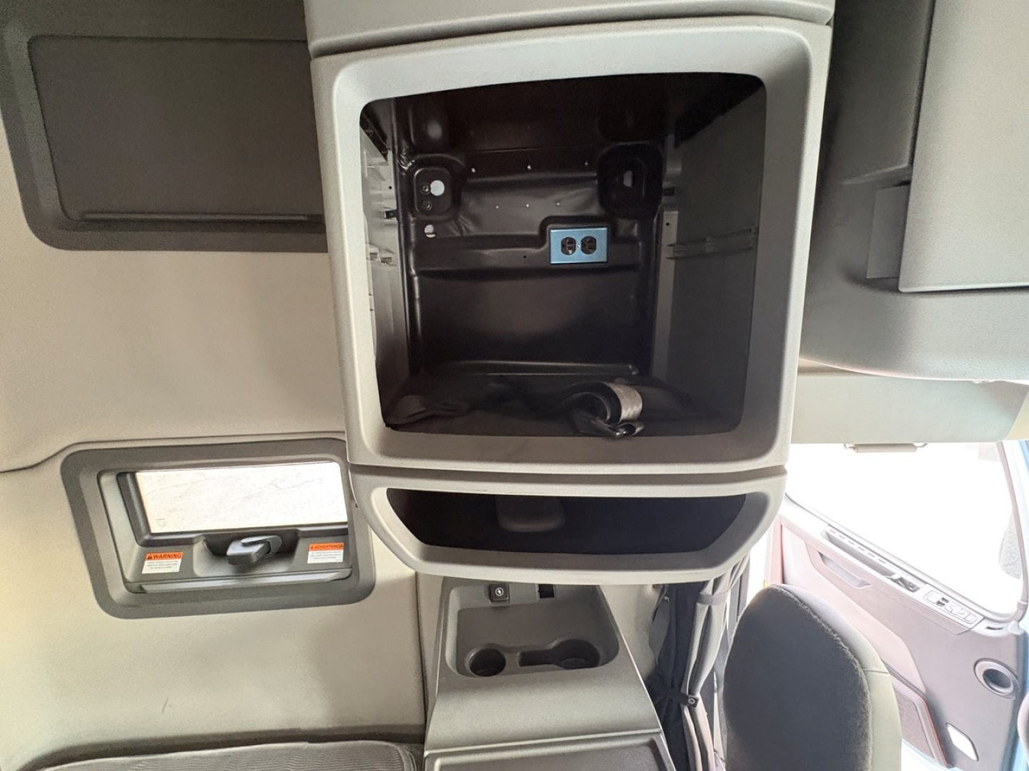 Volvo VNL cab interior showing storage compartment with blue ports and control panel, overhead area, and dashboard window edge.