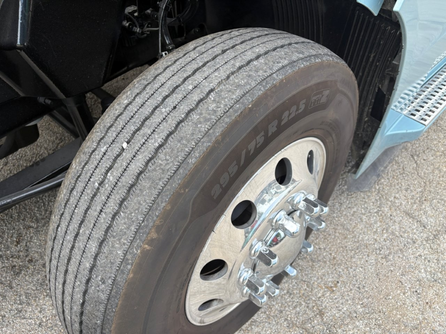 Front wheel of a Volvo VNL truck showing Pirelli or Bridgestone dual tires with wheel hub, lug nuts, and part of the blue fender; visible tread and sidewall markings.