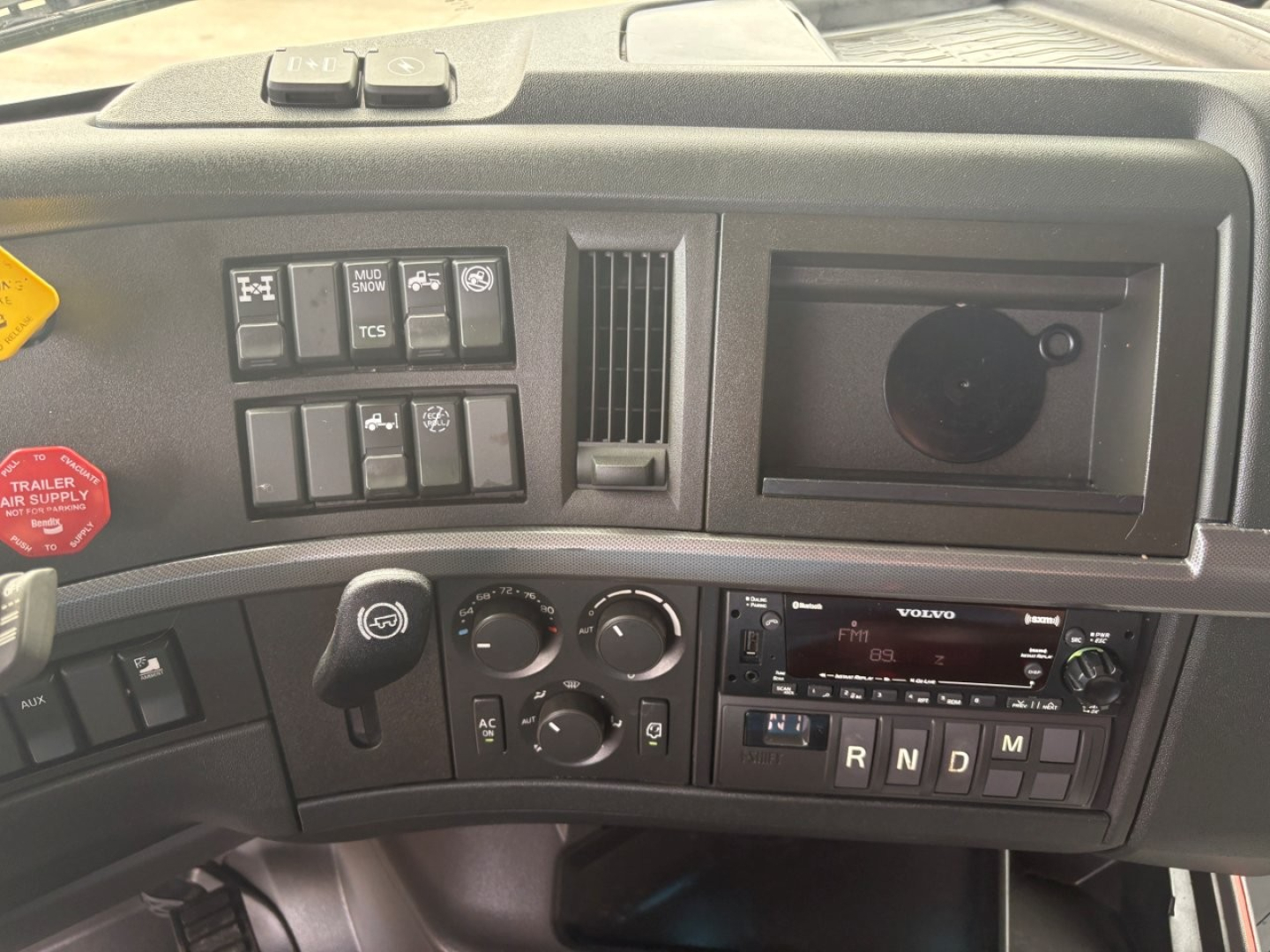 Volvo VNL64T760 dash panel showing climate controls, radio, and gear selector; multiple switches and empty cup holder area visible.