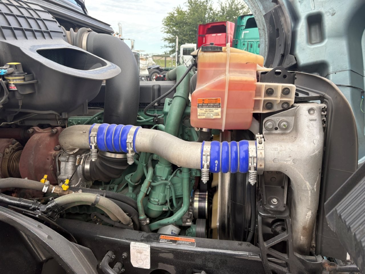 Volvo VNL64T760 engine bay showing blue silicone hoses, orange coolant reservoir, metal turbocharger housing, and intake plumbing.