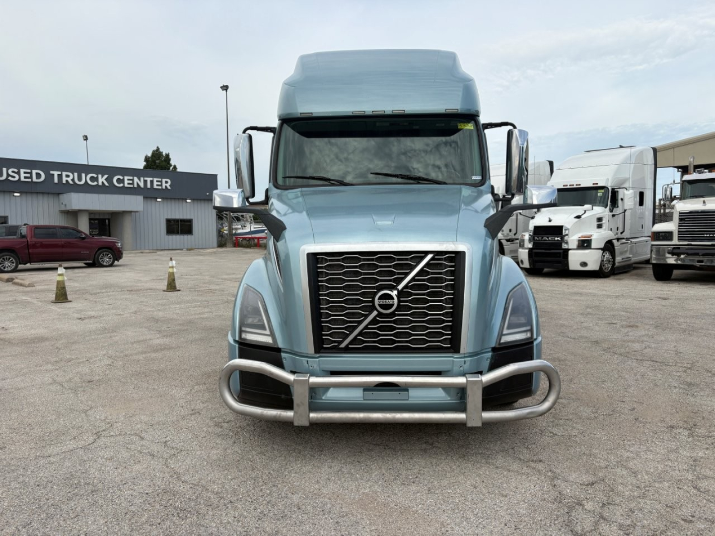 Front view of a light blue Volvo VNL64T760 truck showing grille, bumper guard, and windscreen; visible are Volvo emblem and large chrome grille with twin vertical headlights.