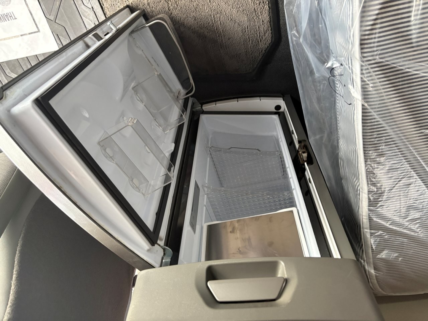 Truck interior showing a compact refrigerator/freezer with lid open, inside cargo area of a 2022 Volvo VNL64T760 sleeper cab.