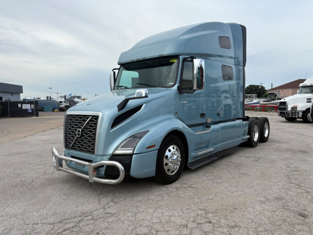 Volvo VNL64T760 truck in a parking lot, light blue exterior, front bull bar, sleeper cab, dual rear axles, chrome mirrors, Volvo emblem on grille.