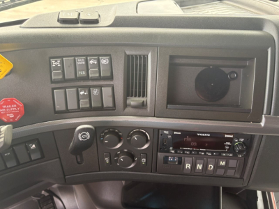 Volvo VNL64T760 dash panel showing climate controls, radio, and gear selector; multiple switches and empty cup holder area visible.