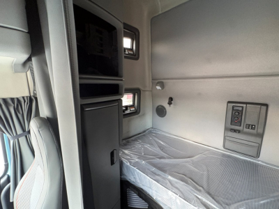 Truck sleeper cab interior with bunk bed area, control panel, and storage compartments.