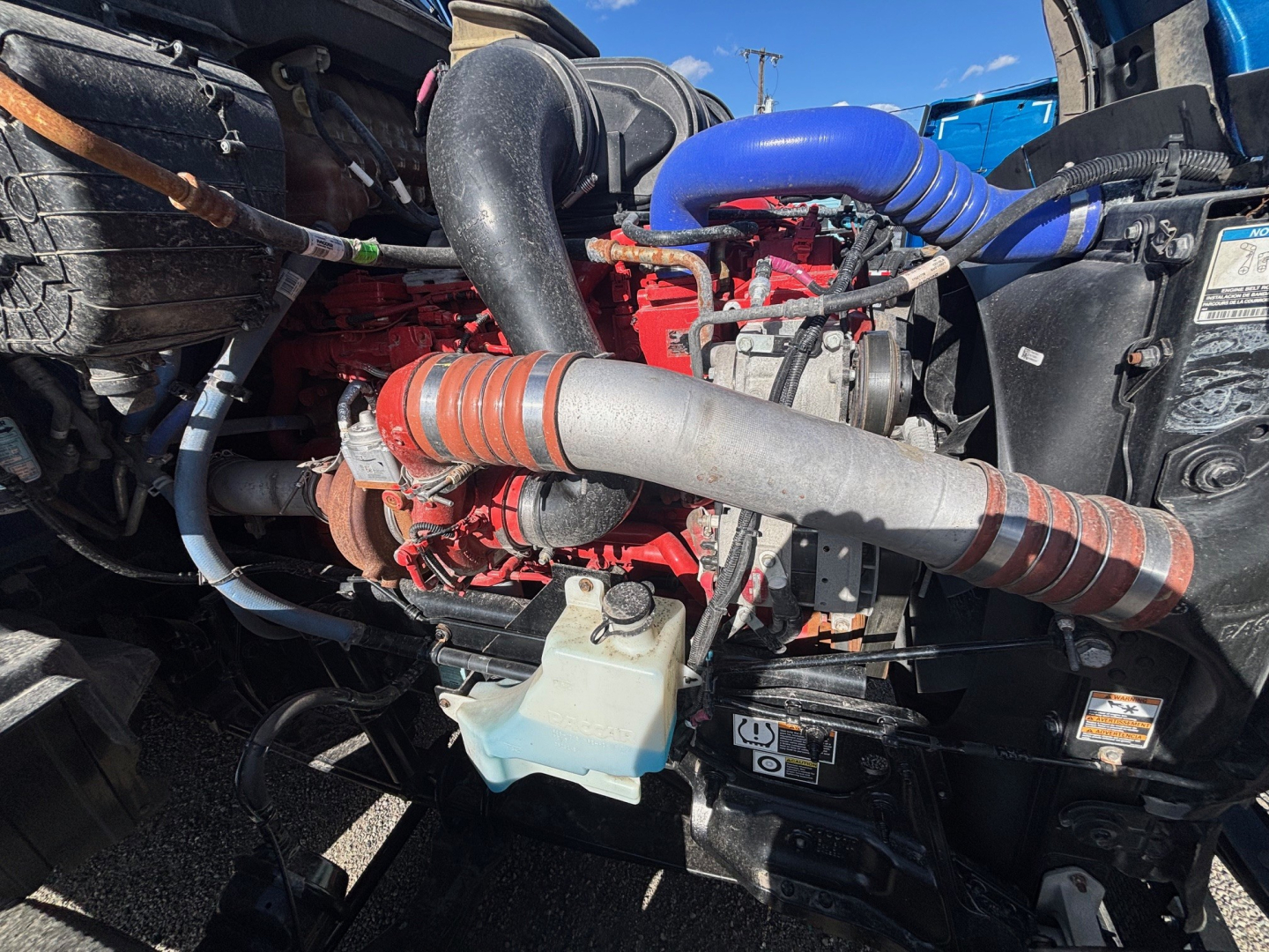 Truck engine bay with red engine block, blue silicone turbo pipe, coolant reservoir, and various hoses and cables visible.