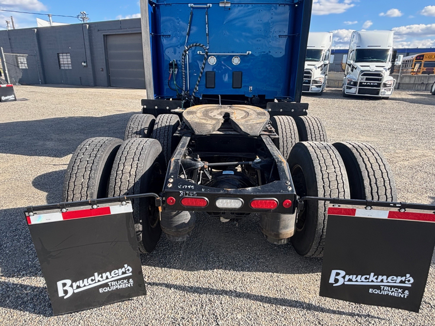 Peterbilt 579 rear view showing fifth wheel and dual rear axles with mud flaps and spare components, blue cab in background.