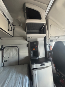 Cab interior of a 2022 Peterbilt 579 showing the dashboard console, storage compartments, and sleeper area with compartments and seating visible.