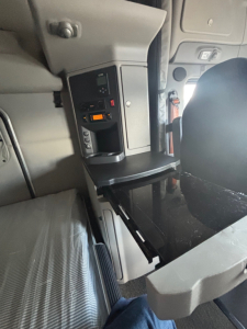 Cab interior of a Peterbilt 579 truck showing a fold-out workspace tray and control panel with small digital display.