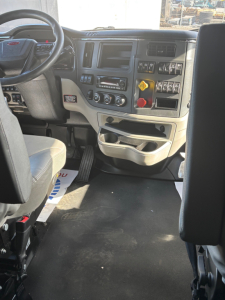 Peterbilt 579 dashboard and driver area showing steering wheel, dashboard controls, and center console with switches and gauges.