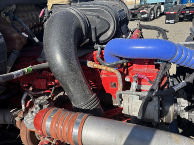 Peterbilt 579 engine bay showing large black intake duct, red engine components, blue silicone hose, silver turbo, and various hoses and wiring.