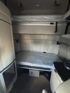 Peterbilt 579 sleeper cab interior showing bunk area with mattress, side cabinets, and overhead storage.