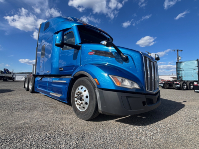 Blue Peterbilt 579 truck, front-left view in a dealership lot, shows sleeper cab, chrome grille, black bumper, and white wheels.