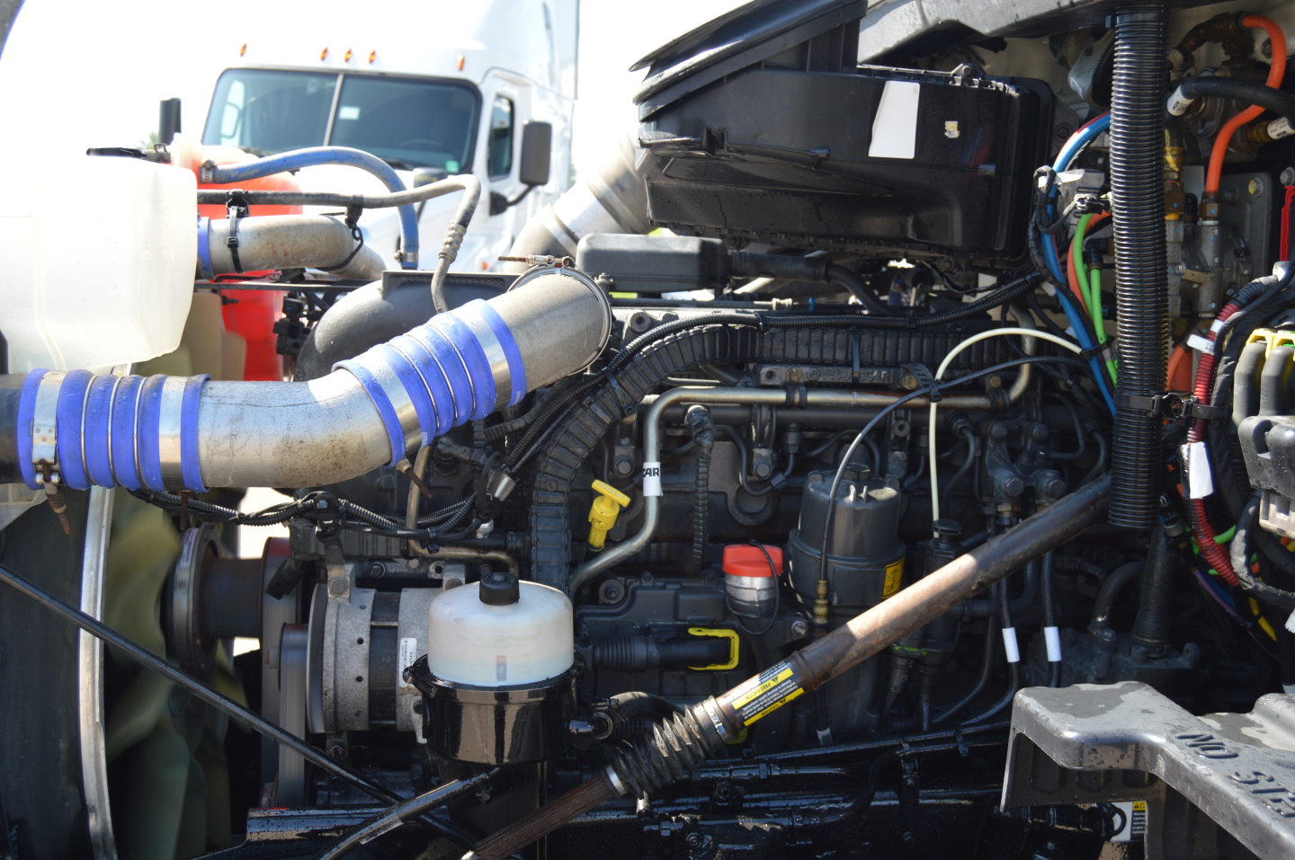 Peterbilt 579 engine bay showing air intake hose, coolant reservoir, and various hoses and wiring in serviceable condition.