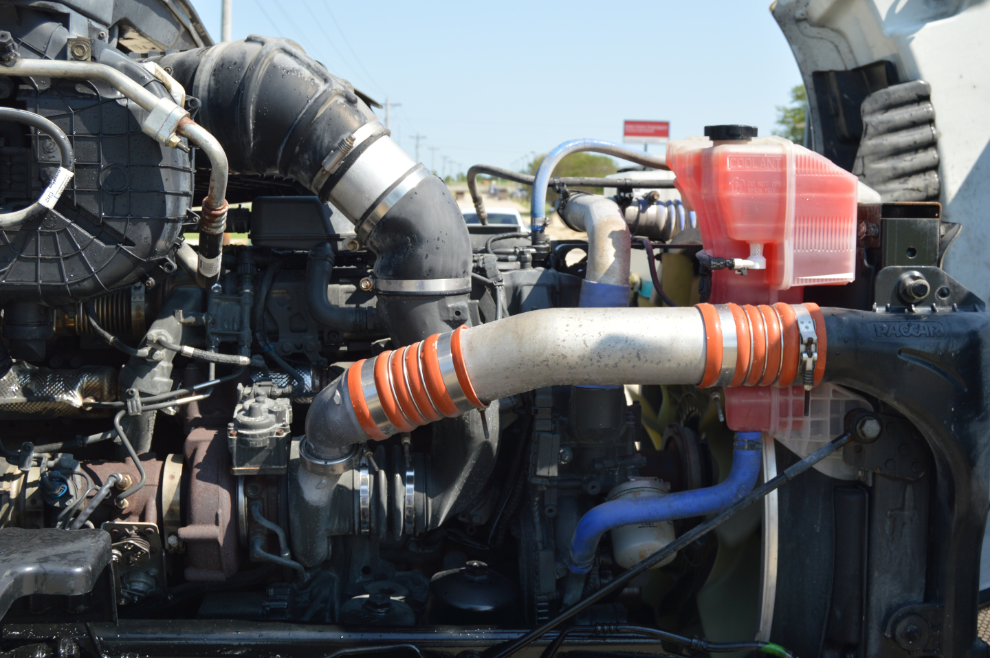 Peterbilt 579 engine bay showing coolant reservoir and intercooler hoses with orange heat wrap and various engine components.