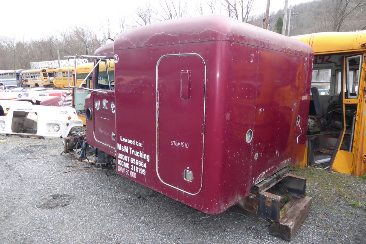 Peterbilt 379 cab-over engine area with maroon sleeper cab shell, side door, and rear hitch; visible stock numbers and white text on side.