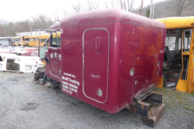 Peterbilt 379 cab-over engine area with maroon sleeper cab shell, side door, and rear hitch; visible stock numbers and white text on side.