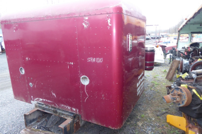 Peterbilt engine bay or cabinet with maroon exterior showing riveted metal panels and two circular openings; side view with rear hitch and surrounding yard equipment.