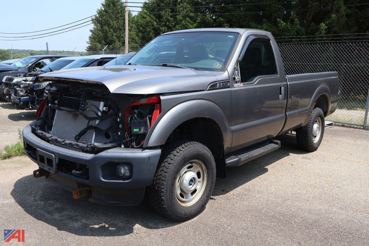 Ford F-250 Super Duty pickup truck with front-end damage showing open hood area and exposed radiator, gray two-door cab, long bed, (2012 model) in a used vehicle lot.