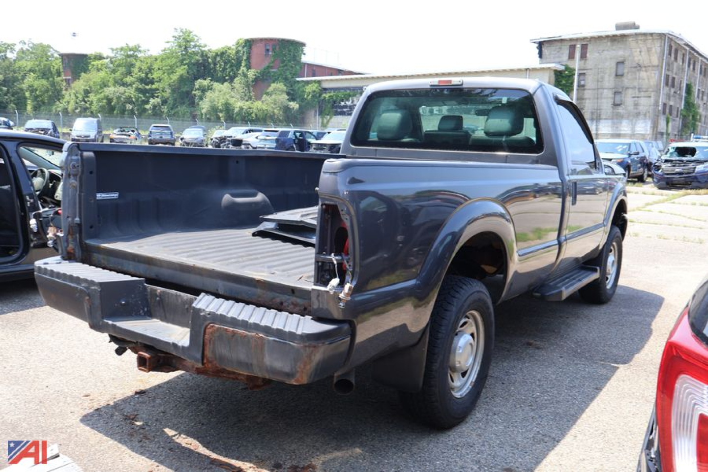 Ford F-250 Super Duty pickup truck in a used lot, rear view showing an empty bed, extended cab, gray/blue paint.