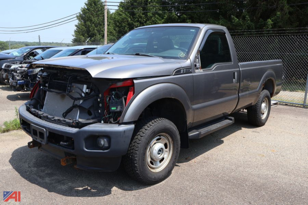Ford F-250 Super Duty pickup truck with front-end damage showing open hood area and exposed radiator, gray two-door cab, long bed, (2012 model) in a used vehicle lot.