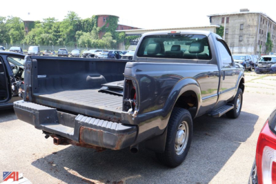 Ford F-250 Super Duty pickup truck in a used lot, rear view showing an empty bed, extended cab, gray/blue paint.