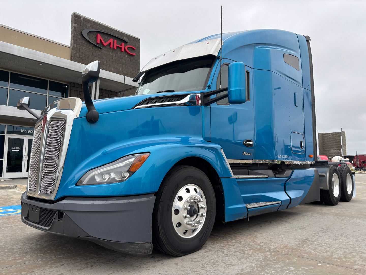 Kenworth T680 tractor-trailer in blue exterior with long hood and sleeper cab, front left view at dealership.