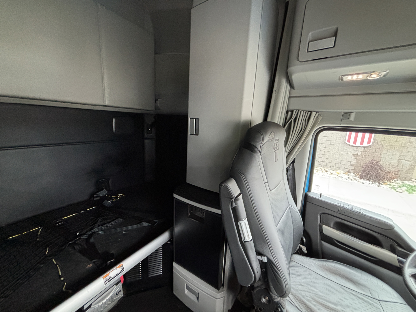 Kenworth T680 truck interior cab view focusing on driver seat and sleeper area with overhead cabinets and dashboard.
