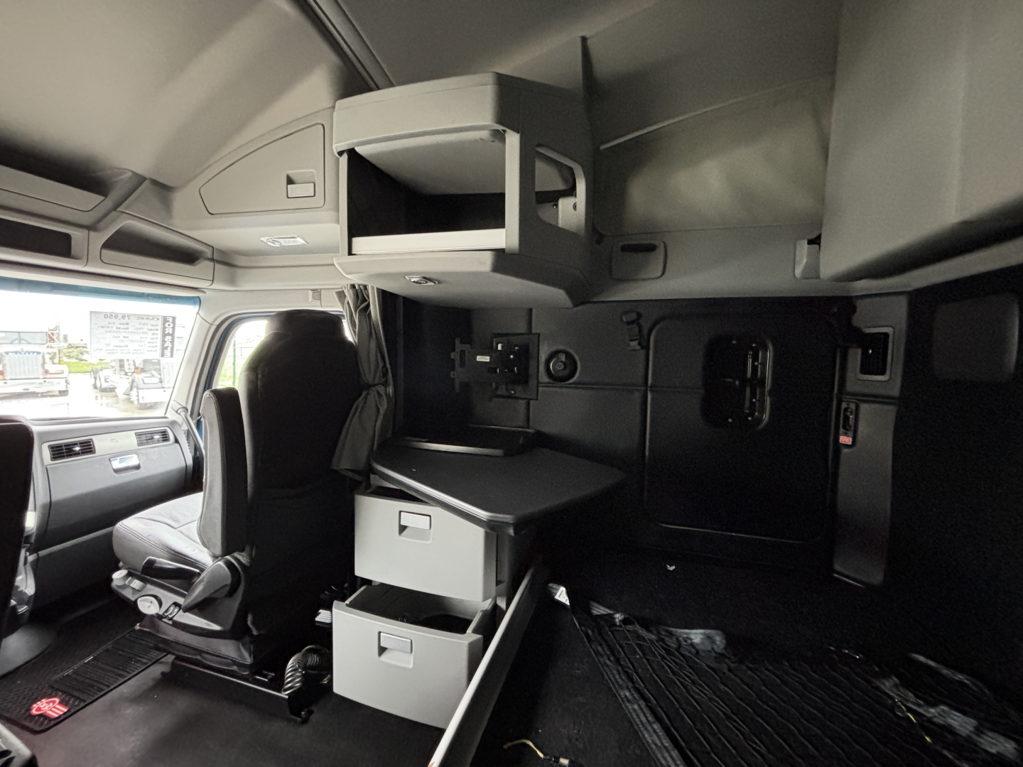Kenworth T680 sleeper cab interior showing overhead storage and filing drawers with a driver's seat and dashboard visible.