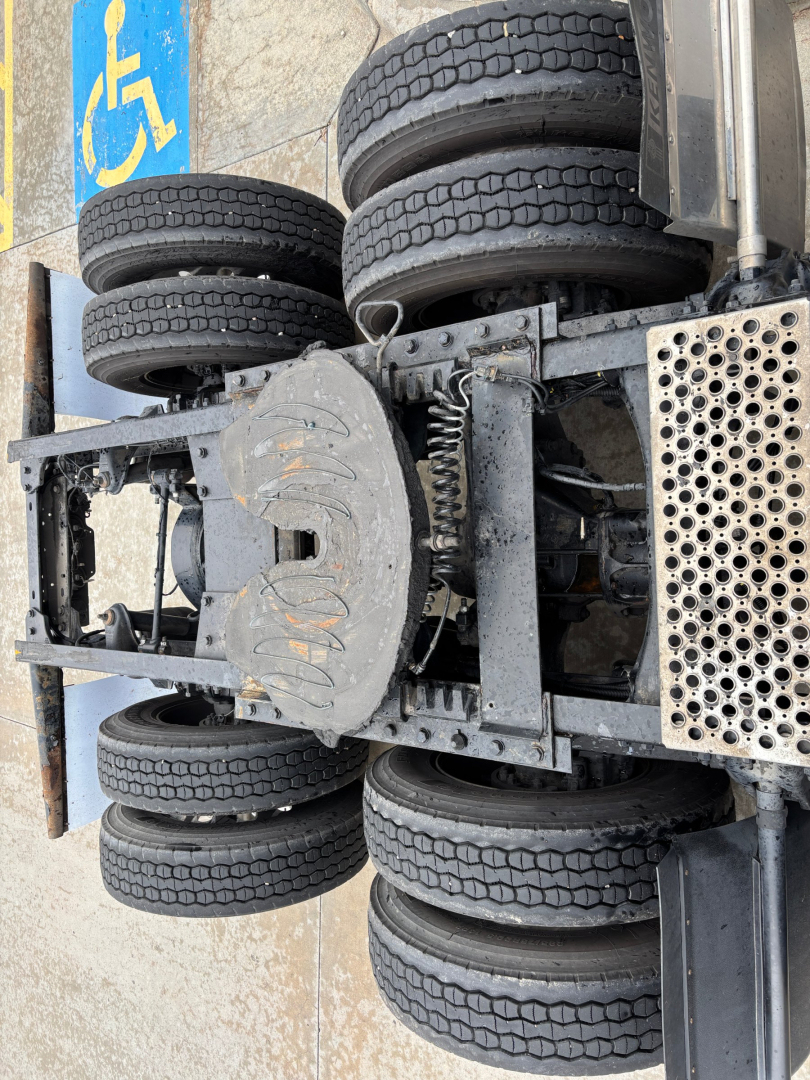 Truck chassis view showing dual rear axles and spare tires on a Kenworth T680, with visible metal framework and a perforated steel platform.