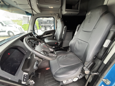 Kenworth T680 cab interior showing driver seat and steering wheel with control panels; front windshield and side mirror visible.