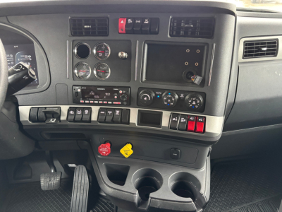 Dashboard of a Kenworth truck showing gauges, switches, and controls with warning buttons, two circular dials, and a row of labeled switches.